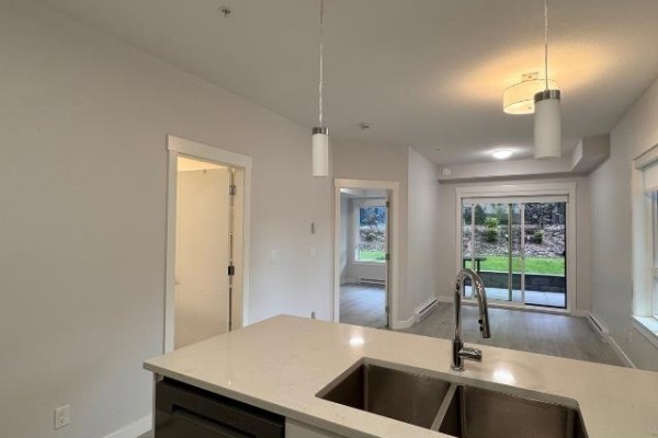 Interior view showing a kitchen island with sink, leading to a living area and patio. - 112 33886 Pine, Abbotsford