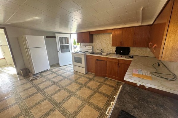 Kitchen with white appliances, wooden cabinets, checkered tile floor, and white countertop. - 112 Anderson Street E, Plumas