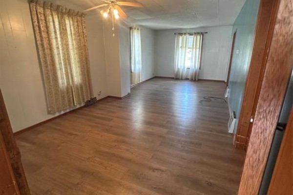 Living room with light brown wood-look flooring, beige curtains, and white paneled walls. - 112 Anderson Street E, Plumas