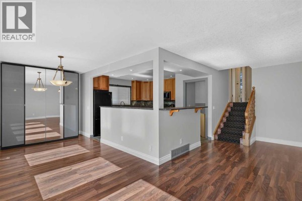 View of the open-concept living area with a breakfast bar, stairs, and mirrored closet doors. - 112 Beaconsfield Rise Nw, Calgary