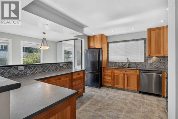 Kitchen with wooden cabinets, dark countertops, stainless steel appliances, and tiled flooring. - 112 Beaconsfield Rise Nw, Calgary