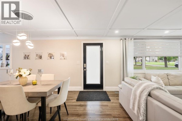 Living room area with a sectional sofa, dining area, and a door leading outside. Wood floors throughout. - 112 Clovelly, Tecumseh