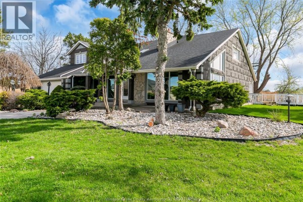 Side view of the house showing stone and dark siding, large windows, and landscaping with rocks and grass. - 112 County Rd 22, Belle River