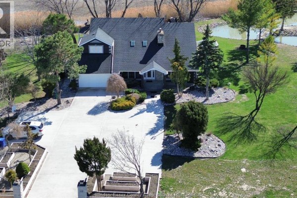 Concrete driveway with decorative flowerbeds and stone pillars, leading towards a subdivision with houses and trees. - 112 County Rd 22, Belle River