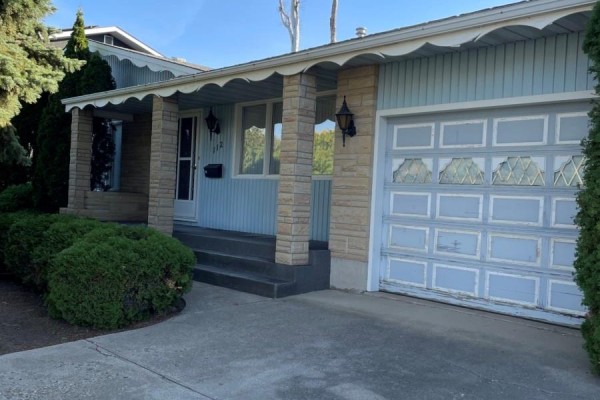 Close-up of the home's entrance with a light blue door, stone accents, and a garage door. - 112 Deborah Crescent, Saskatoon