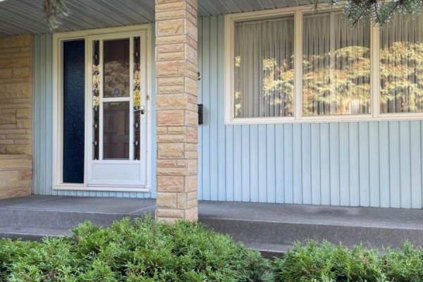 Entrance detail showing the screen door, stone pillar, and a window reflecting trees. - 112 Deborah Crescent, Saskatoon