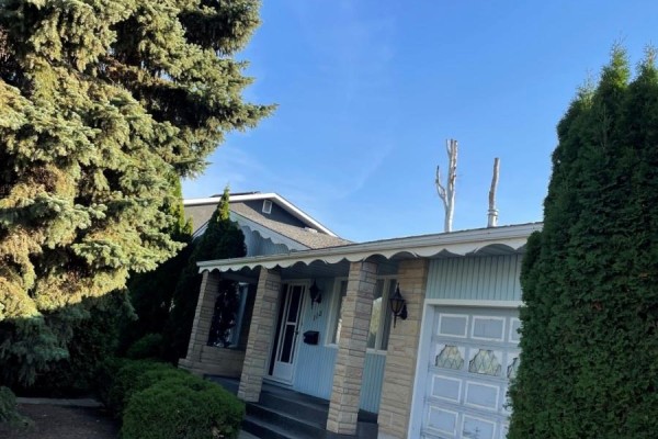 Side exterior view of the house showing the entrance, garage, and dense evergreen trees. - 112 Deborah Crescent, Saskatoon