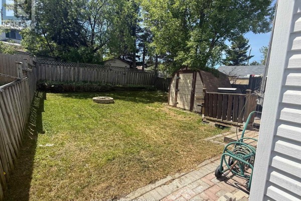 Backyard with a wooden fence, a shed, a fire pit, and a patio. - 112 Dwyer Avenue, Timmins