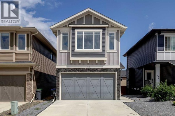 Front exterior of a two-story home with grey siding, stone accents, and a large grey garage door. - 112 Emberside Place, Cochrane