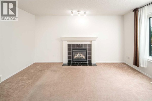 Living room with a beige carpet and a view of the fireplace and window. - 112 Everridge Drive Sw, Calgary
