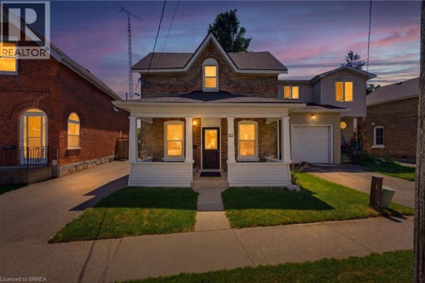 Front exterior of a brick house at dusk, with warm lights illuminating the windows and porch. - 112 Grand River Avenue, Brantford