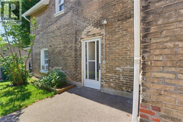 Rear exterior of a brick house with a white-framed glass door and a small paved patio area. - 112 Grand River Avenue, Brantford