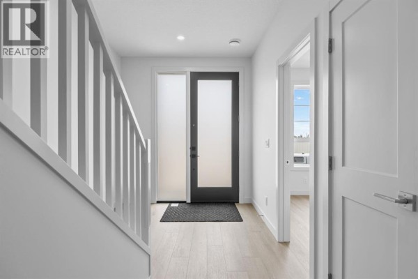 Interior entryway with white walls, light wood floors, and a frosted glass door. - 112 Greenwich Drive Nw, Calgary