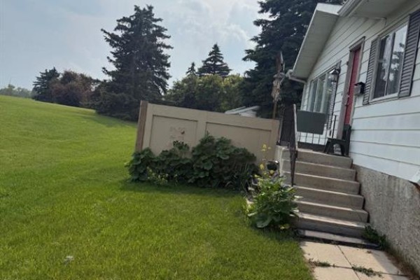Exterior view of white house entrance with red door, metal railings, and concrete steps. - 112 Huntstrom Drive Ne, Calgary