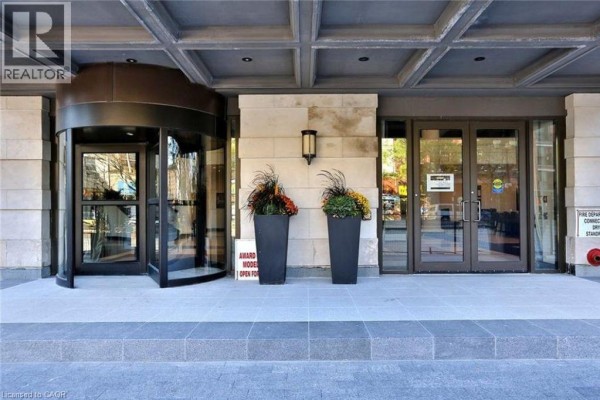 Close-up of building entrance with revolving door, double glass doors, and planters. - 112 King Street Unit# 1105, Hamilton