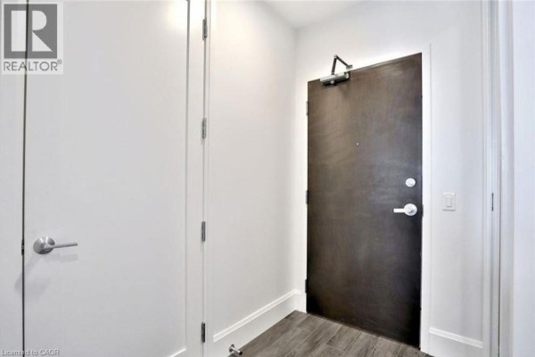 Interior hallway with a dark brown apartment door and adjacent closet doors, both with silver handles. - 112 King Street Unit# 1105, Hamilton