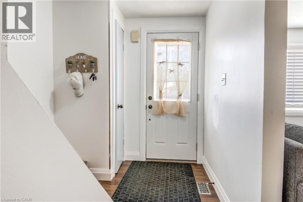 Townhouse entrance hallway with white door, dark doormat, wood flooring, and coat hooks. - 112 Richardson Drive Unit# 24, Port Dover