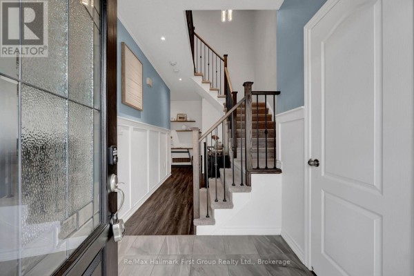 Foyer with glass front door, wood-look flooring, and staircase to the upper level. - 112 Roy Nichols Drive, Clarington