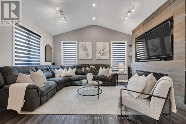 Living room with large sectional sofa, coffee table, and mounted television on wood accent wall. - 112 Roy Nichols Drive, Clarington