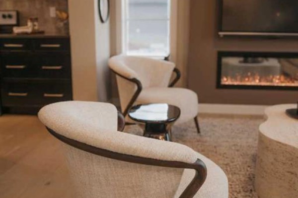 Living room seating area with two cream chairs, a dark side table, and fireplace. - 112 Southbow Avenue, Cochrane
