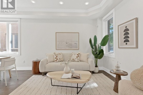 Living room featuring a cream sofa, coffee table, and decorative art on a white wall. - 112 Southbrook Crescent, Markham