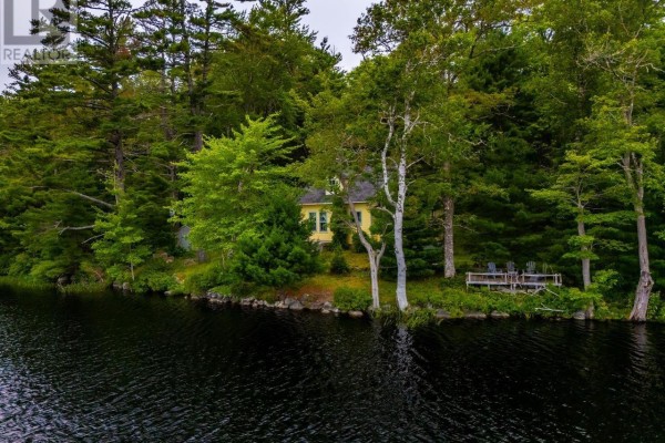 A yellow house with a red chimney sits on the edge of a dark lake, surrounded by mature trees. - 112 Thomas Lake Road, Milford
