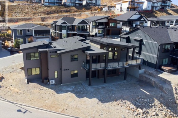 Side and rear view of a multi-level modern home with glass railings and dark siding. - 1120 Collinson Court, Kelowna