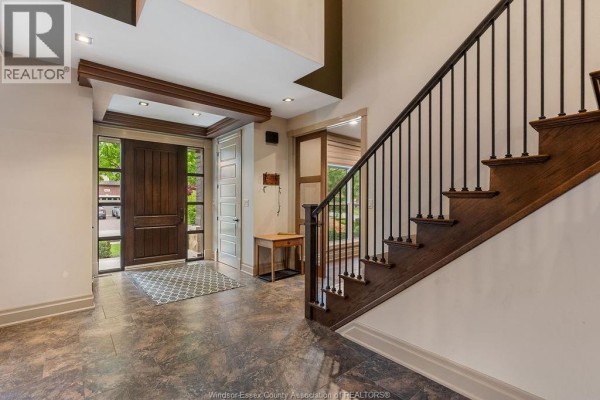 Foyer with wood front door, patterned grey entryway rug, and dark wood staircase with black spindles. - 1120 Deerview, Lasalle