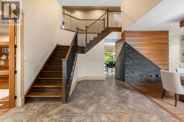 Interior view of a spacious foyer with a grand dark wood staircase and stacked stone accent wall. - 1120 Deerview, Lasalle