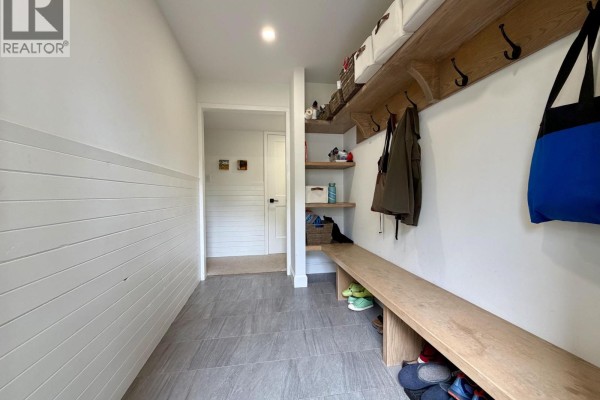 Interior entryway with white shiplap walls, tiled floor, wooden bench, and shelving. - 1120 Toronto Street, Smithers
