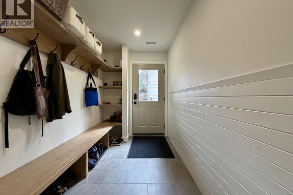 Entryway with a light-colored door, tiled floor, shiplap walls, wooden bench, and storage. - 1120 Toronto Street, Smithers