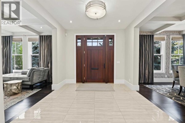 Spacious foyer with a dark wood front door, beige tiled floor, and large windows. - 1121 Valois Avenue Sw, Calgary