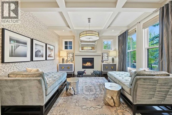 Living room with a fireplace, coffered ceiling, patterned wallpaper, and two grey velvet benches. - 1121 Valois Avenue Sw, Calgary