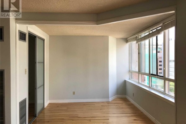 Empty room with hardwood floors and large bay windows. - 1122 - 633 Bay Street, Toronto