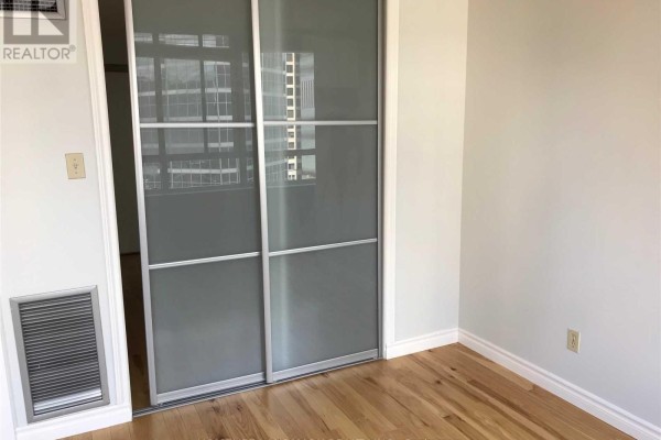 Room interior with hardwood floors and sliding mirrored closet doors. - 1122 - 633 Bay Street, Toronto