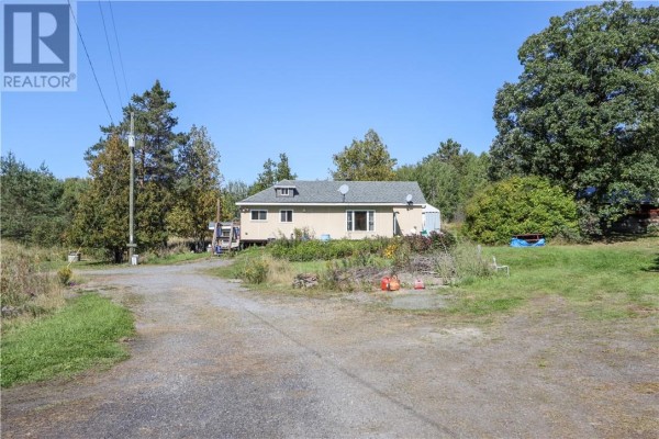 View of the rear of the house from a gravel driveway, surrounded by trees. - 1123 Regional Road 10, Whitefish