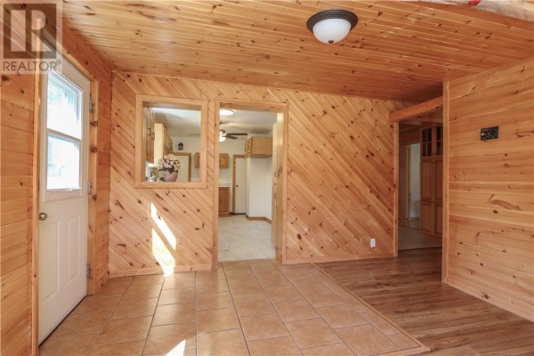 Interior room with light wood paneling on walls and ceiling, tiled floor, and doorway to kitchen. - 1123 Regional Road 10, Whitefish