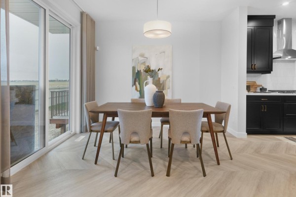 Dining table with six chairs set in a dining area with large windows and artwork. - 1124 Cristall Cr Sw, Edmonton