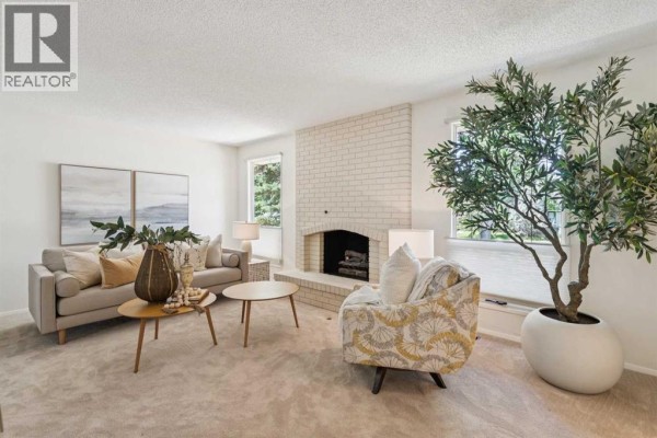 Living room with a cream brick fireplace, beige sofa, armchair, and two round coffee tables. - 11248 Braeside Drive Sw, Calgary