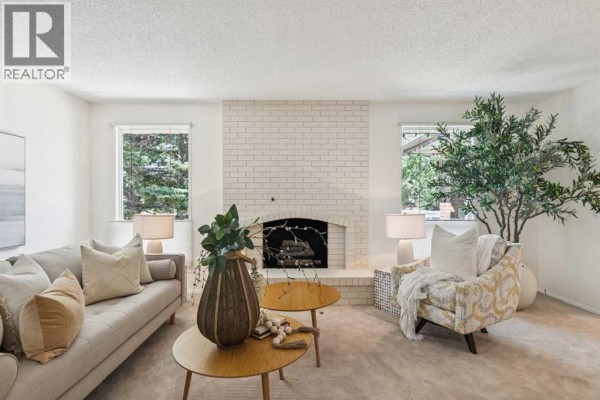 Living room featuring a cream brick fireplace, light grey sofa, decorative armchair, and large potted plant. - 11248 Braeside Drive Sw, Calgary