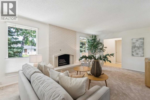 Living room with a fireplace, sofa, armchair, and view into the dining area and kitchen. - 11248 Braeside Drive Sw, Calgary