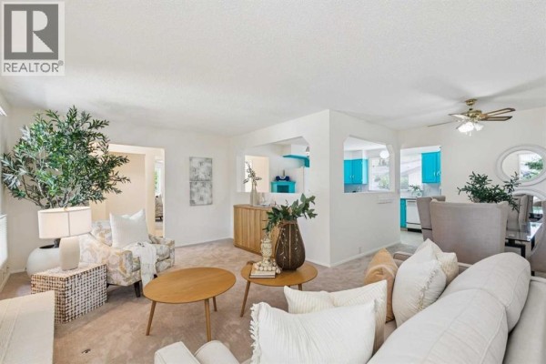 Open-concept living and dining area with neutral-toned furniture and a glimpse of the bright blue kitchen cabinets. - 11248 Braeside Drive Sw, Calgary