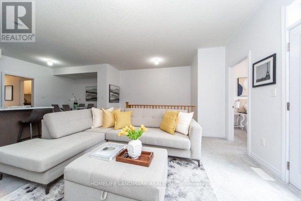 Living room with a sectional sofa, ottoman, fireplace, and view of an open-concept kitchen. - 1126 Baltic Lane, Pickering