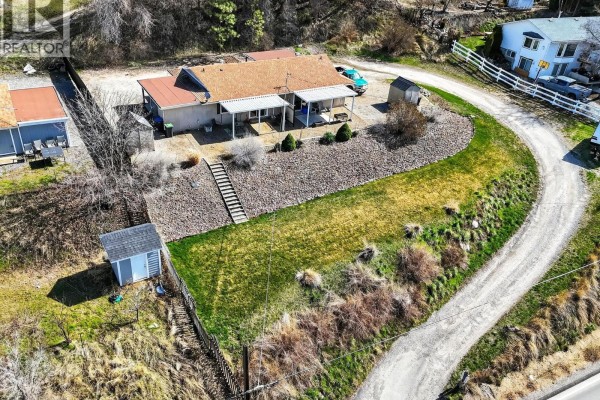Side aerial view of the duplex at 11263 Lodge Road, showing the property's sloped yard with grass and brush. - 11263 Lodge Road, Lake Country