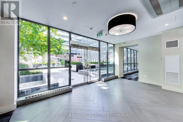 Building lobby with large windows looking out onto a courtyard, grey floors and modern lighting. - 113 - 38 Iannuzzi Street, Toronto