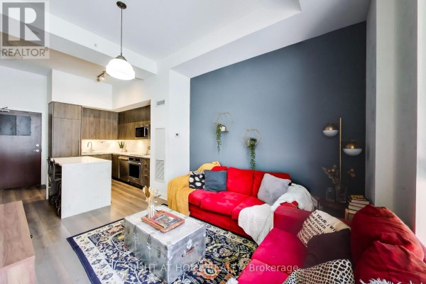 Open concept living room and kitchen with a red sofa, island, and dark grey accent wall. - 113 - 38 Iannuzzi Street, Toronto
