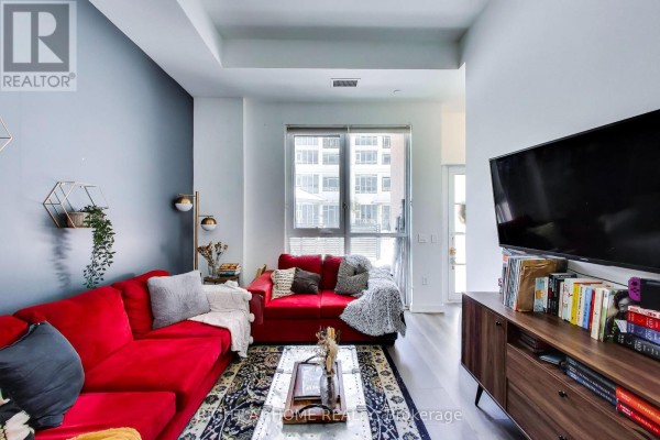 Living room with a red sofa, coffee table, and media console with a large television. - 113 - 38 Iannuzzi Street, Toronto