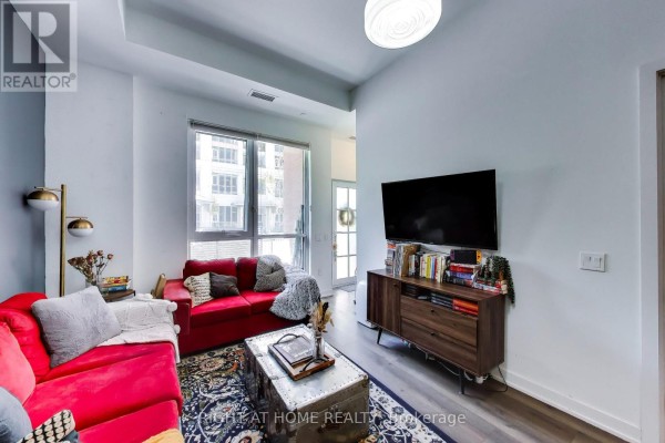 Living room with a red sectional sofa, coffee table, and media console facing a window. - 113 - 38 Iannuzzi Street, Toronto