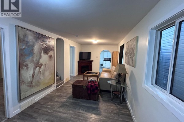 Living room with beige sofa, large painting, fireplace, television, and wood-look flooring. - 113 109th Street W, Saskatoon