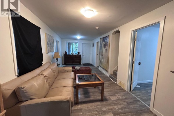 Living room showing beige sofa, coffee table, entryway, and stairs leading down. - 113 109th Street W, Saskatoon